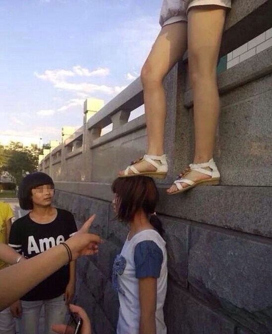 照片中，一穿蓝白短袖的女孩被女孩踩头。